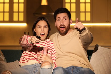 Photo of Emotional couple watching TV with popcorn on sofa