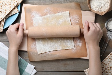 Woman rolling raw dough for traditional matzo at wooden table, top view