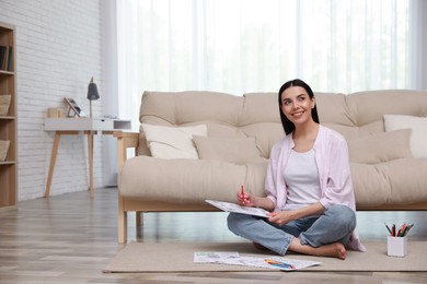 Photo of Young woman coloring antistress page near sofa in living room