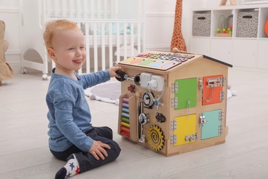 Cute little boy playing with busy board house on floor at home