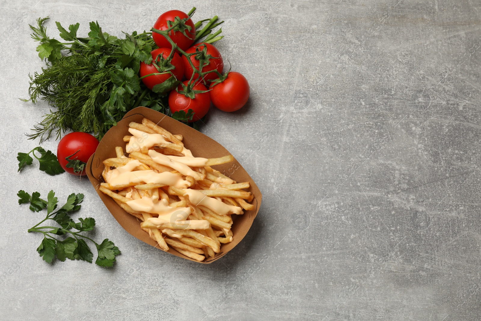 Photo of Tasty potato fries, cheese sauce in paper container and products on grey table, top view. Space for text