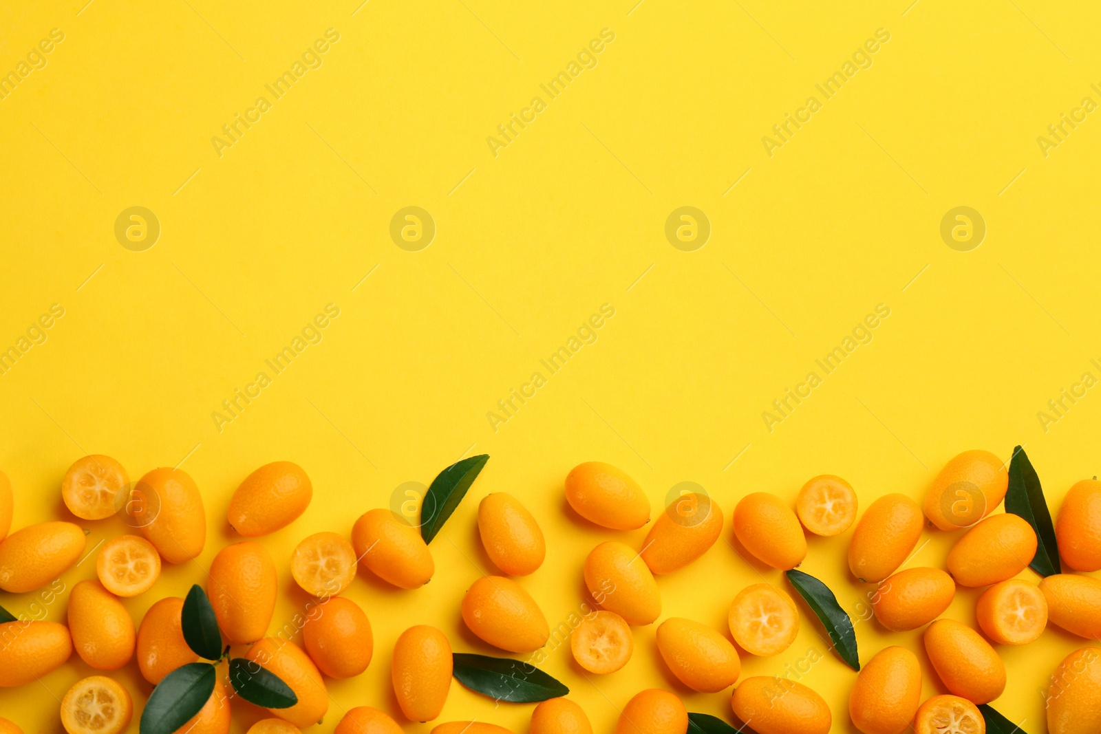 Photo of Fresh ripe kumquats with green leaves on yellow background, flat lay. Space for text