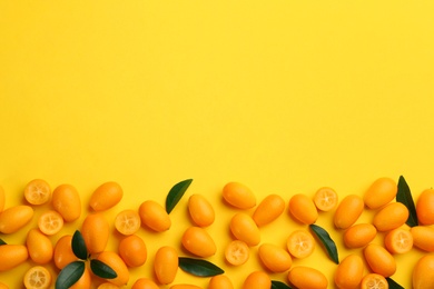 Fresh ripe kumquats with green leaves on yellow background, flat lay. Space for text