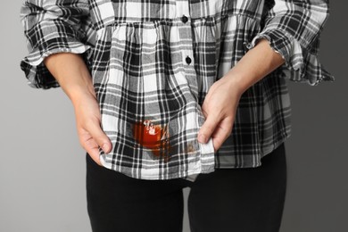 Photo of Woman showing sauce stain on her shirt against grey background, closeup