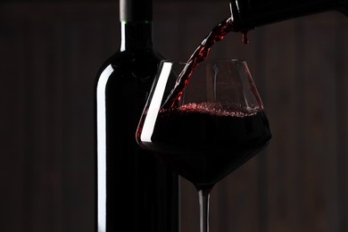 Pouring red wine into glass and bottles against blurred background, closeup