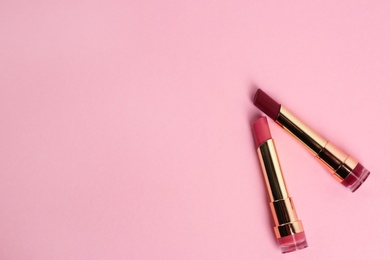 Bright lipsticks in gold tubes on pink background, flat lay. Space for text