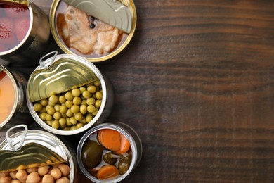 Photo of Open tin cans with different products on wooden table, flat lay. Space for text