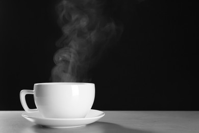 Photo of Cup with steam on table against black background. Space for text