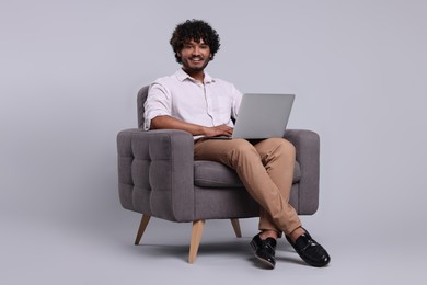 Photo of Smiling man with laptop sitting in armchair on light grey background, space for text