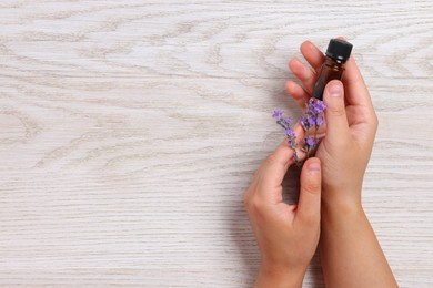 Woman with bottle of lavender essential oil and flowers on wooden background, top view. Space for text