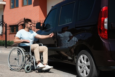 Photo of Young man in wheelchair opening door of his van outdoors
