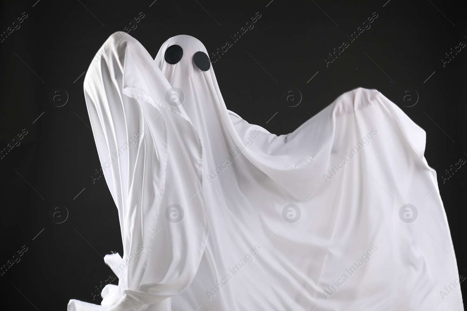 Photo of Creepy ghost. Person covered with white sheet on black background