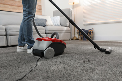 Young man using vacuum cleaner at home, closeup