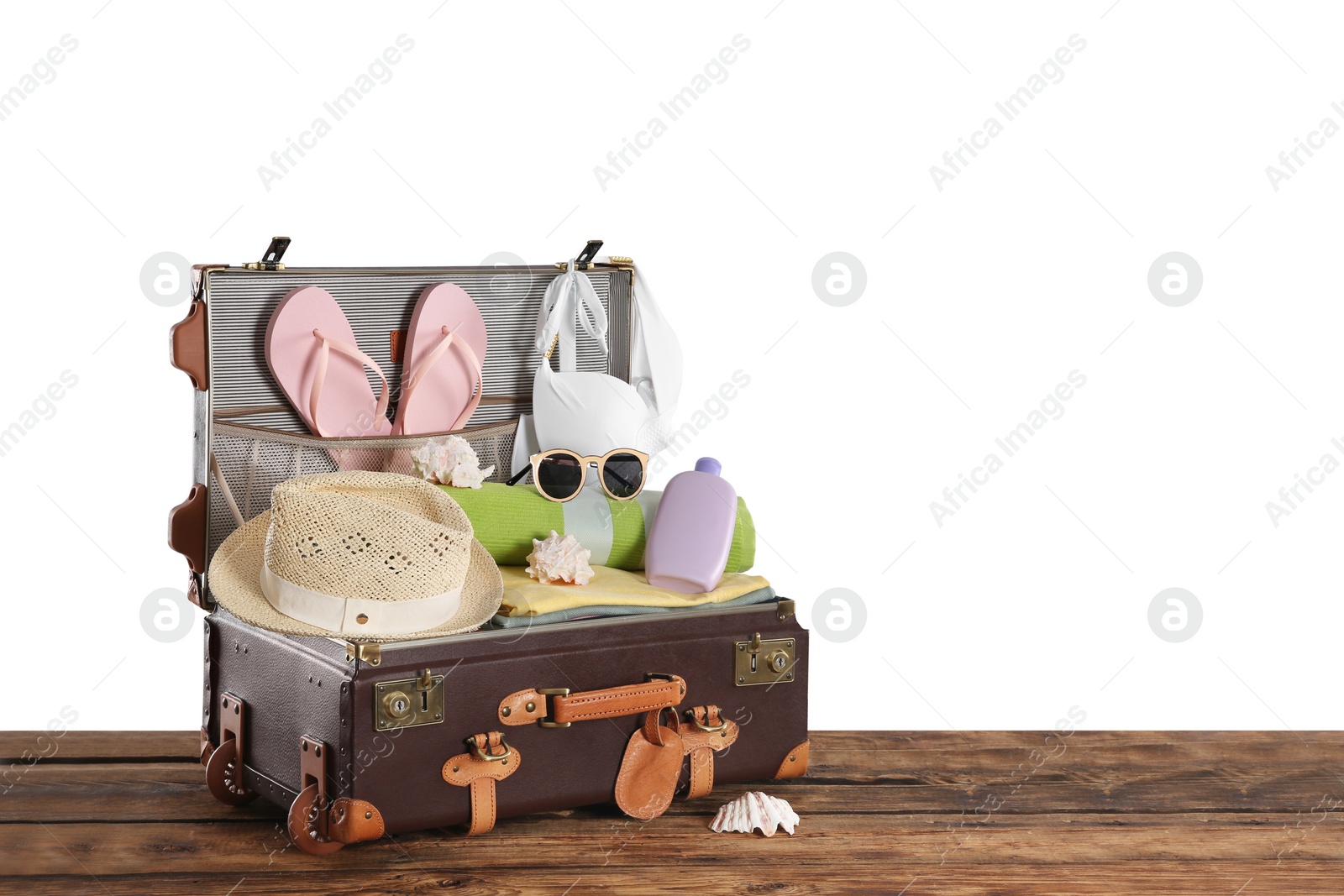 Photo of Open vintage suitcase with different beach objects packed for summer vacation on wooden table against white background