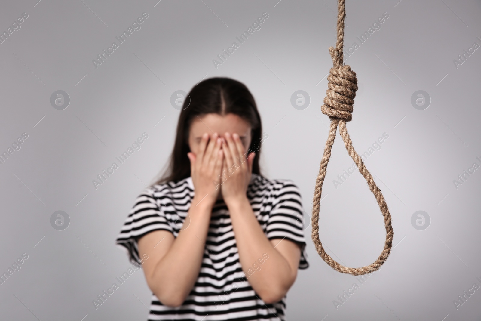 Photo of Depressed woman crying near rope noose on light grey background