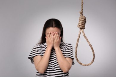 Depressed woman crying near rope noose on light grey background