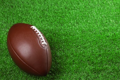 Photo of American football ball on green grass. Space for text