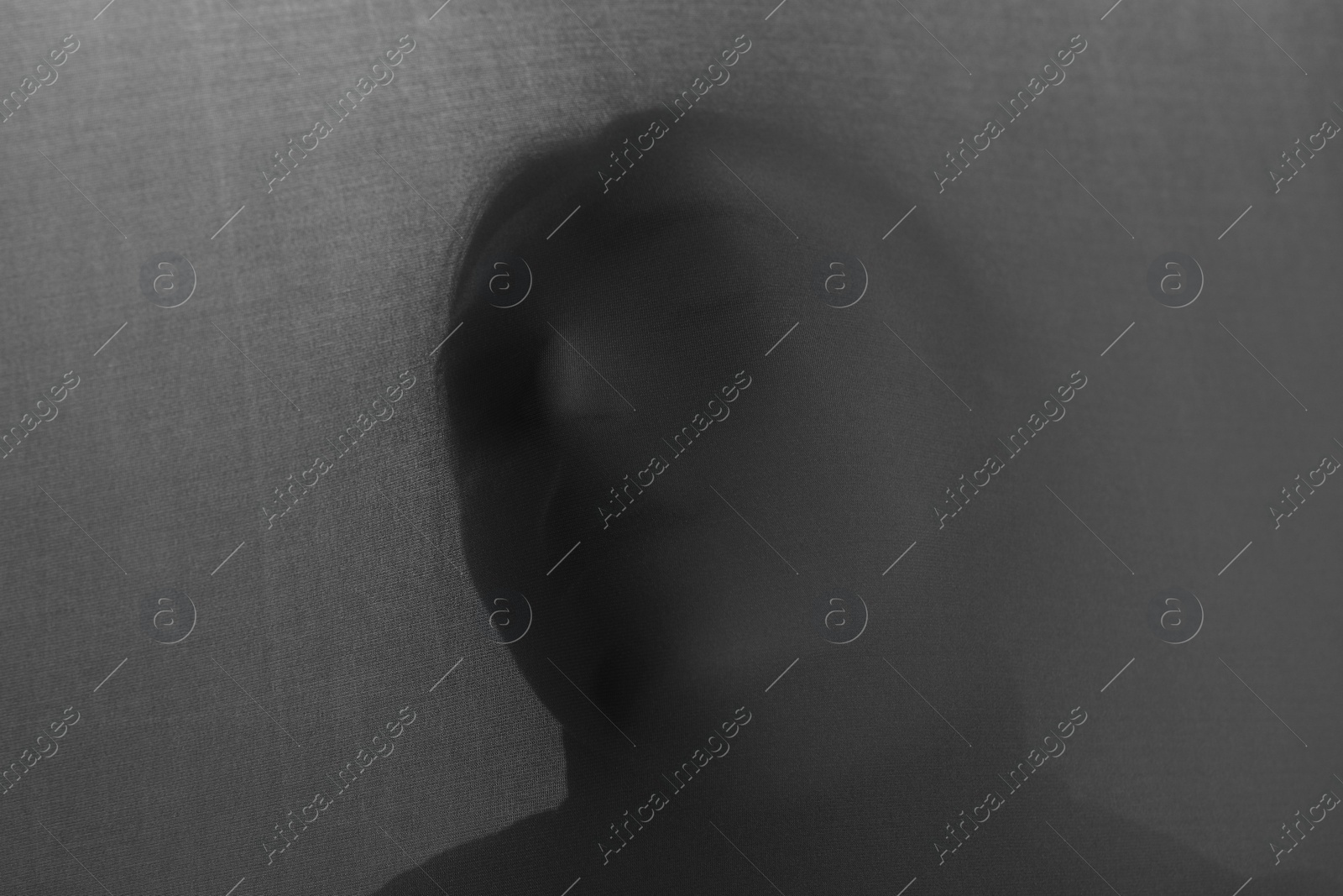 Photo of Silhouette of creepy ghost behind grey cloth. Black and white effect