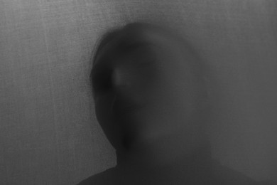 Photo of Silhouette of creepy ghost behind grey cloth. Black and white effect