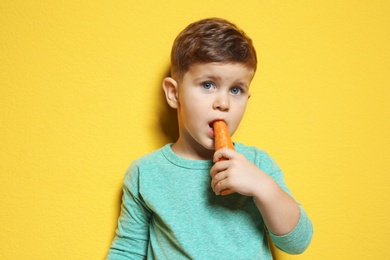 Photo of Adorable little boy eating carrot on color background