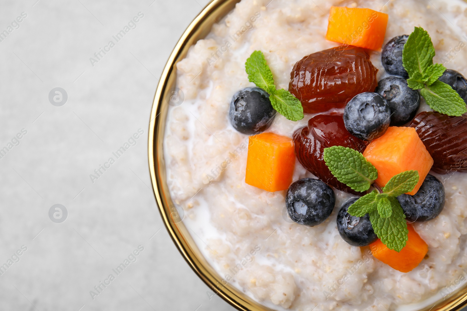 Photo of Delicious barley porridge with blueberries, pumpkin, dates and mint in bowl on grey table, top view. Space for text