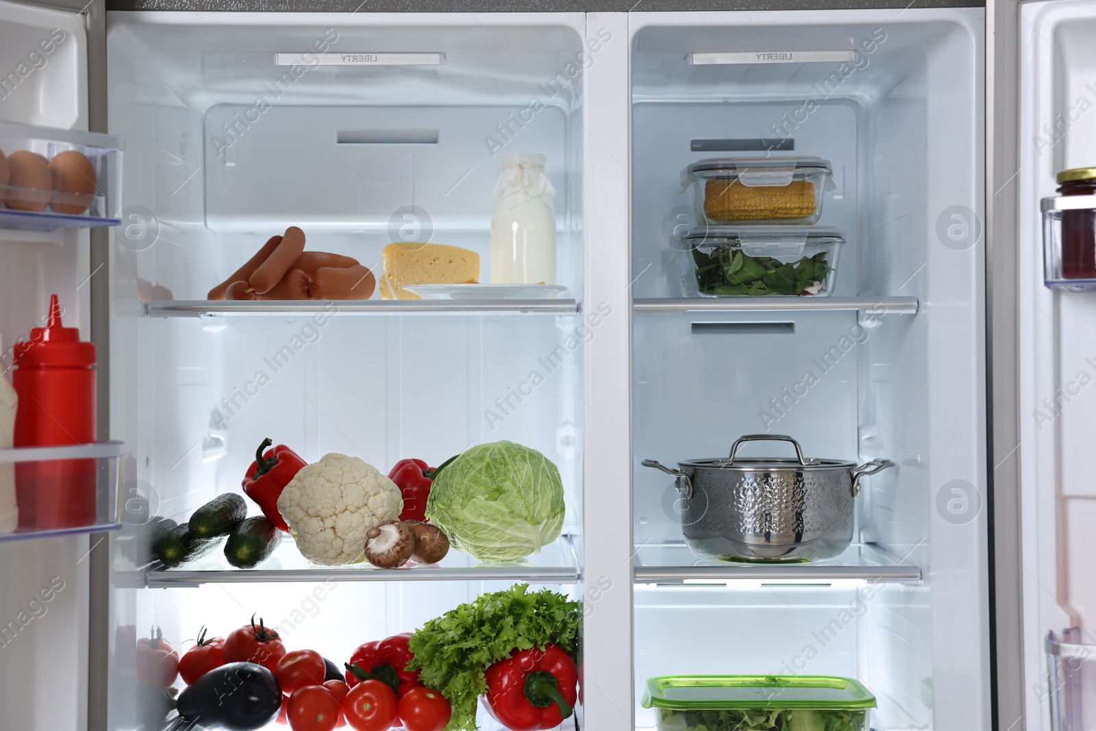 Photo of Open refrigerator full of different products indoors