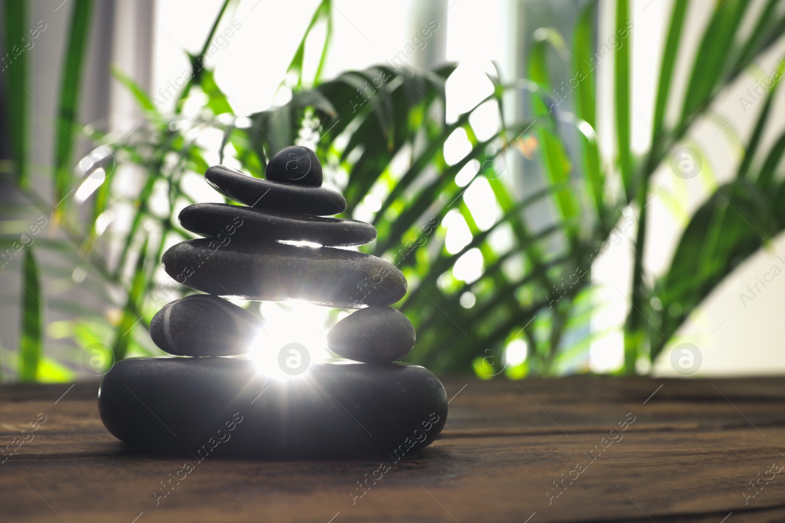 Photo of Table with stack of stones and blurred green leaves on background, space for text. Zen concept