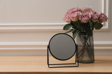 Photo of Mirror and vase with pink roses on wooden dressing table, space for text