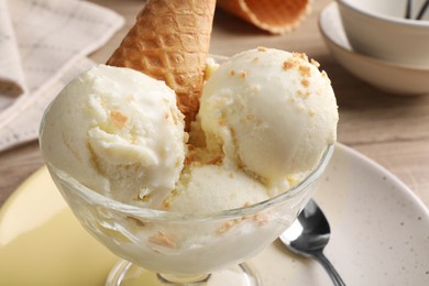 Delicious scoops of vanilla ice cream with wafer cone in glass dessert bowl on table, closeup