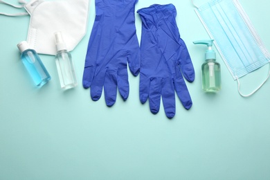 Medical gloves, protective masks and hand sanitizers on light blue background, flat lay. Space for text