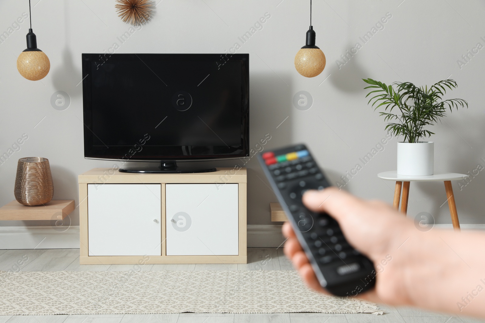 Photo of Young man switching channels on TV set with remote control at home, closeup