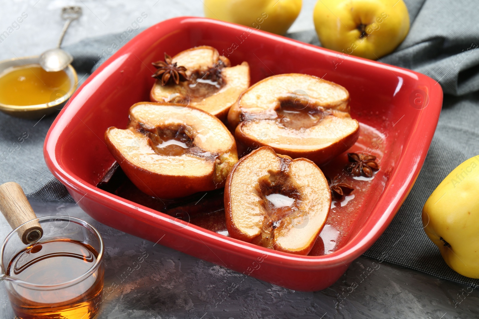 Photo of Tasty baked quinces with honey in dish on grey textured table, closeup