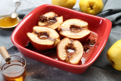 Photo of Tasty baked quinces with honey in dish on grey textured table, closeup