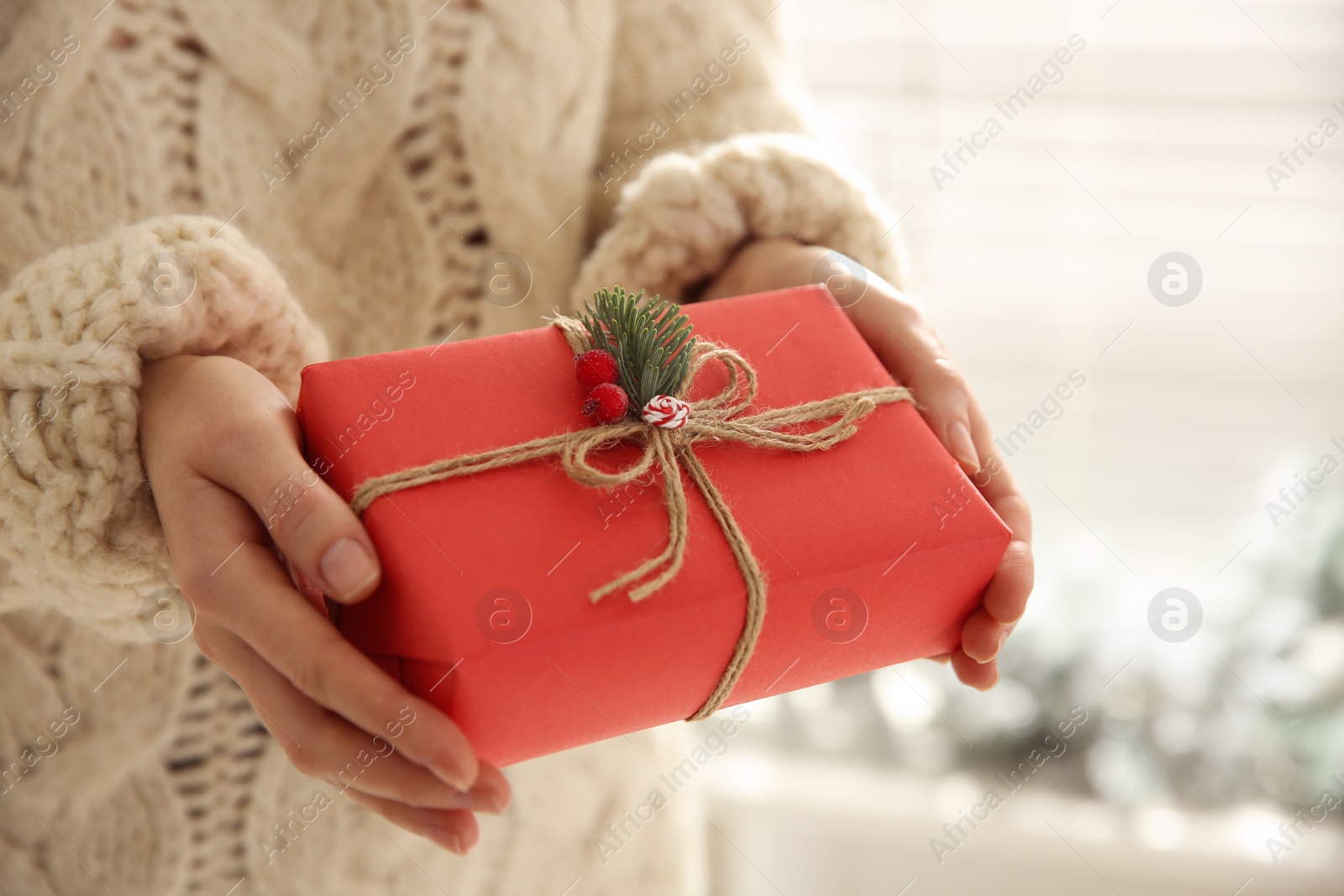 Photo of Woman holding red Christmas gift box indoors, closeup