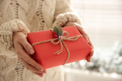 Woman holding red Christmas gift box indoors, closeup