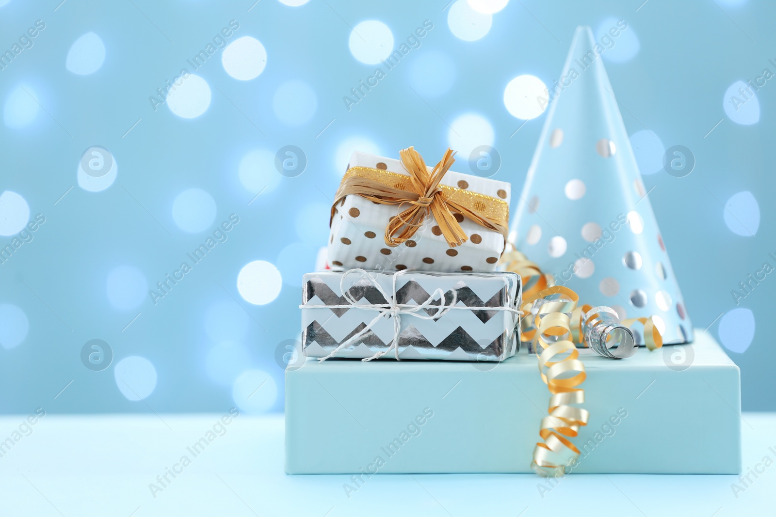 Photo of Gift boxes and party hat on table against blurred lights. Space for text
