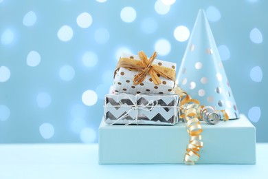 Gift boxes and party hat on table against blurred lights. Space for text