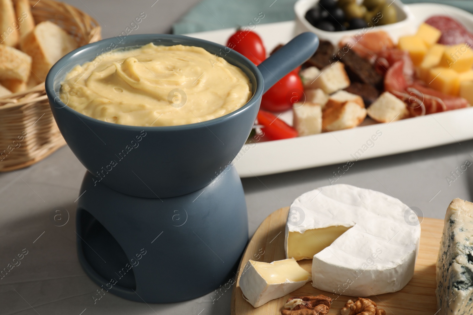 Photo of Fondue with tasty melted cheese and different snacks on grey table