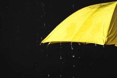 Photo of Opened yellow umbrella under rain against black background, closeup