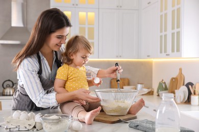 Mother and her little daughter cooking dough together in kitchen