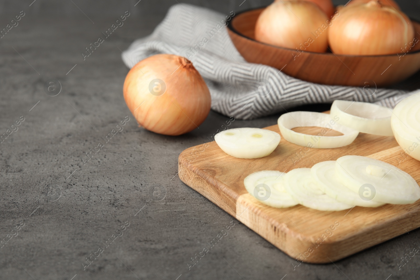 Photo of Wooden board with cut onion and bowl of bulbs on grey table, space for text