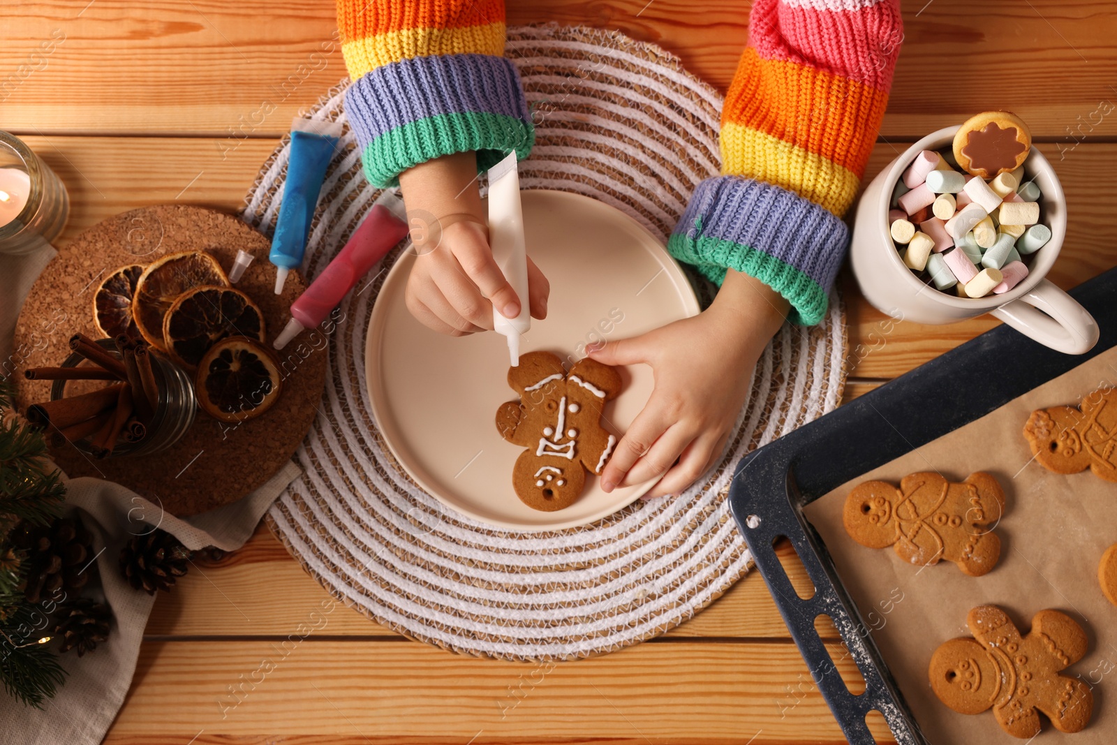Photo of Little child decorating Christmas cookie at wooden table, top view