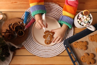 Little child decorating Christmas cookie at wooden table, top view