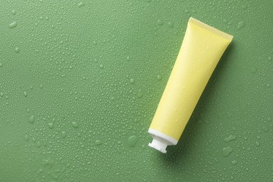 Photo of Moisturizing cream in tube on green background with water drops, top view. Space for text