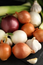 Photo of Fresh onion bulbs, leek and garlic on black table, closeup