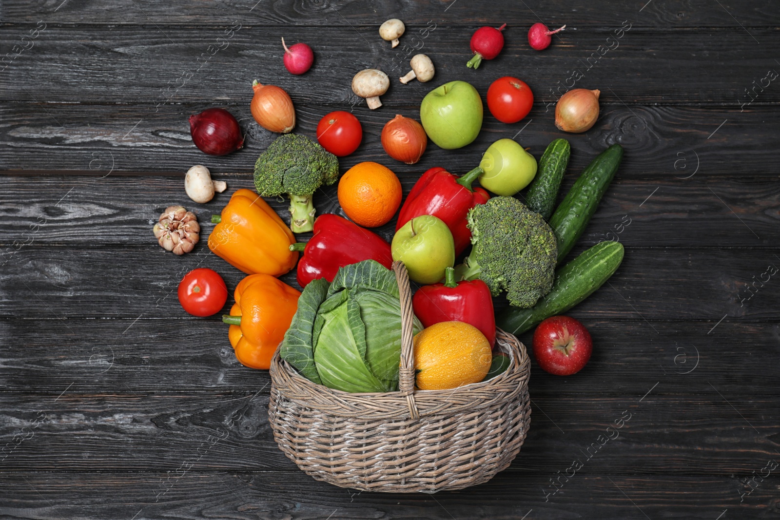 Photo of Basket with scattered fruits and vegetables on black wooden table, flat lay