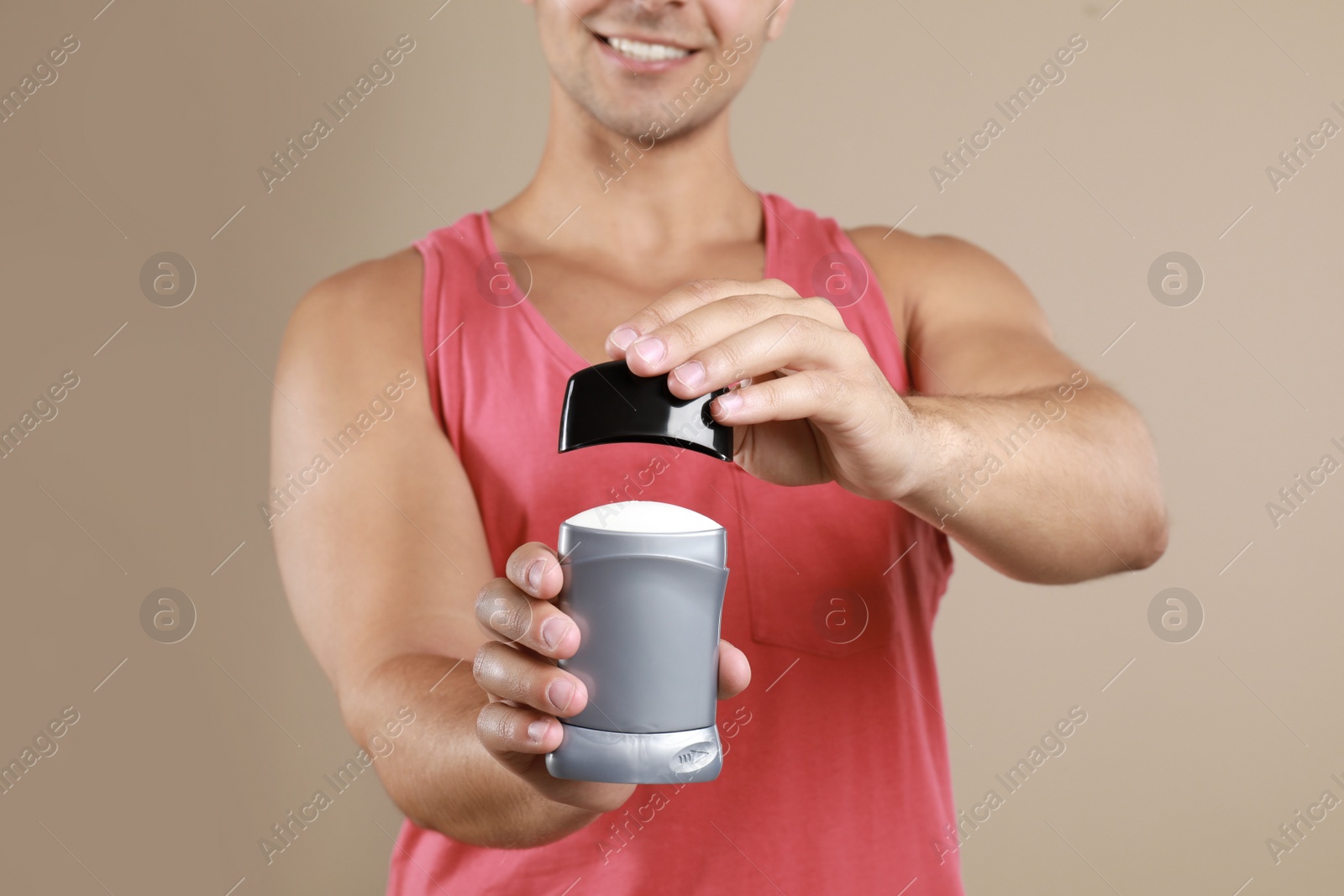 Photo of Young man holding deodorant on beige background, closeup. Mockup for design