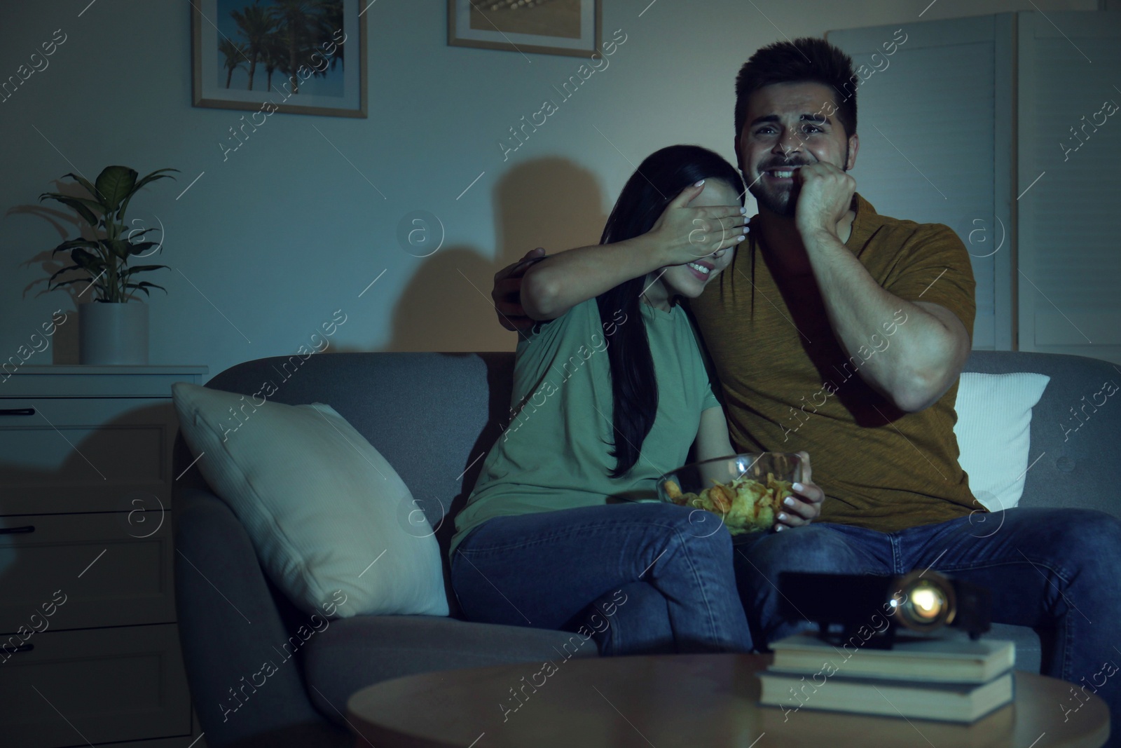 Photo of Emotional young couple watching movie using video projector at home