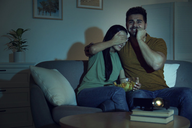 Photo of Emotional young couple watching movie using video projector at home