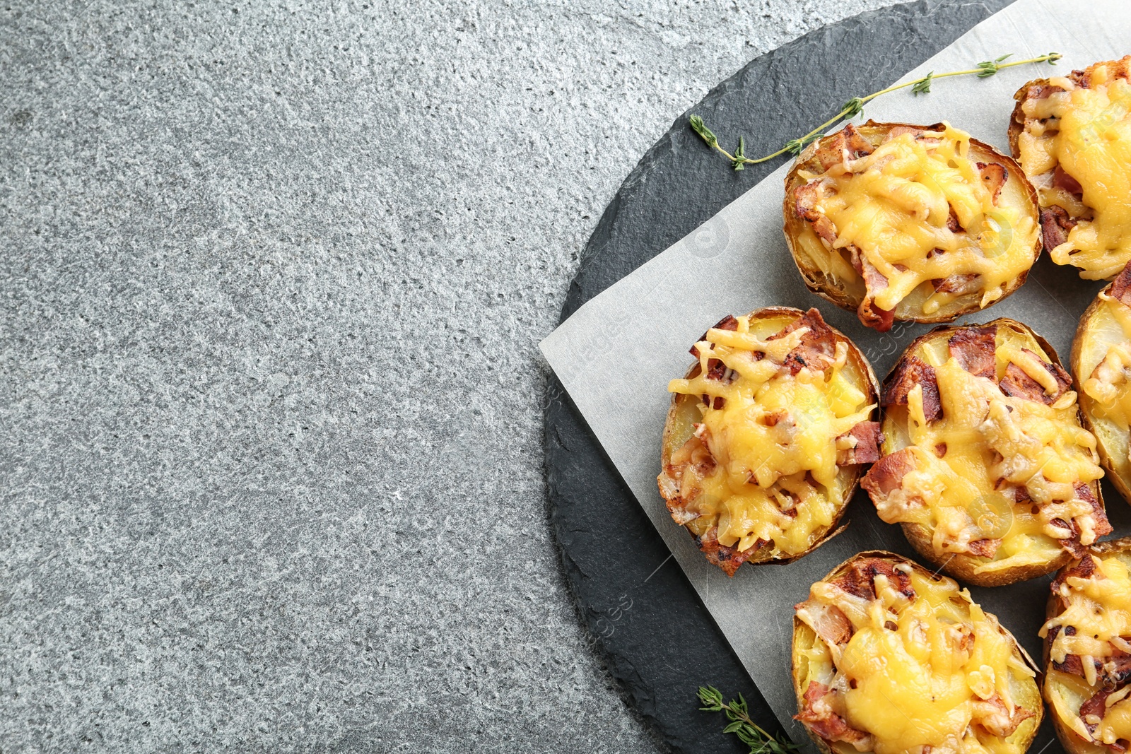 Photo of Slate plate with baked potatoes on grey background, top view with space for text